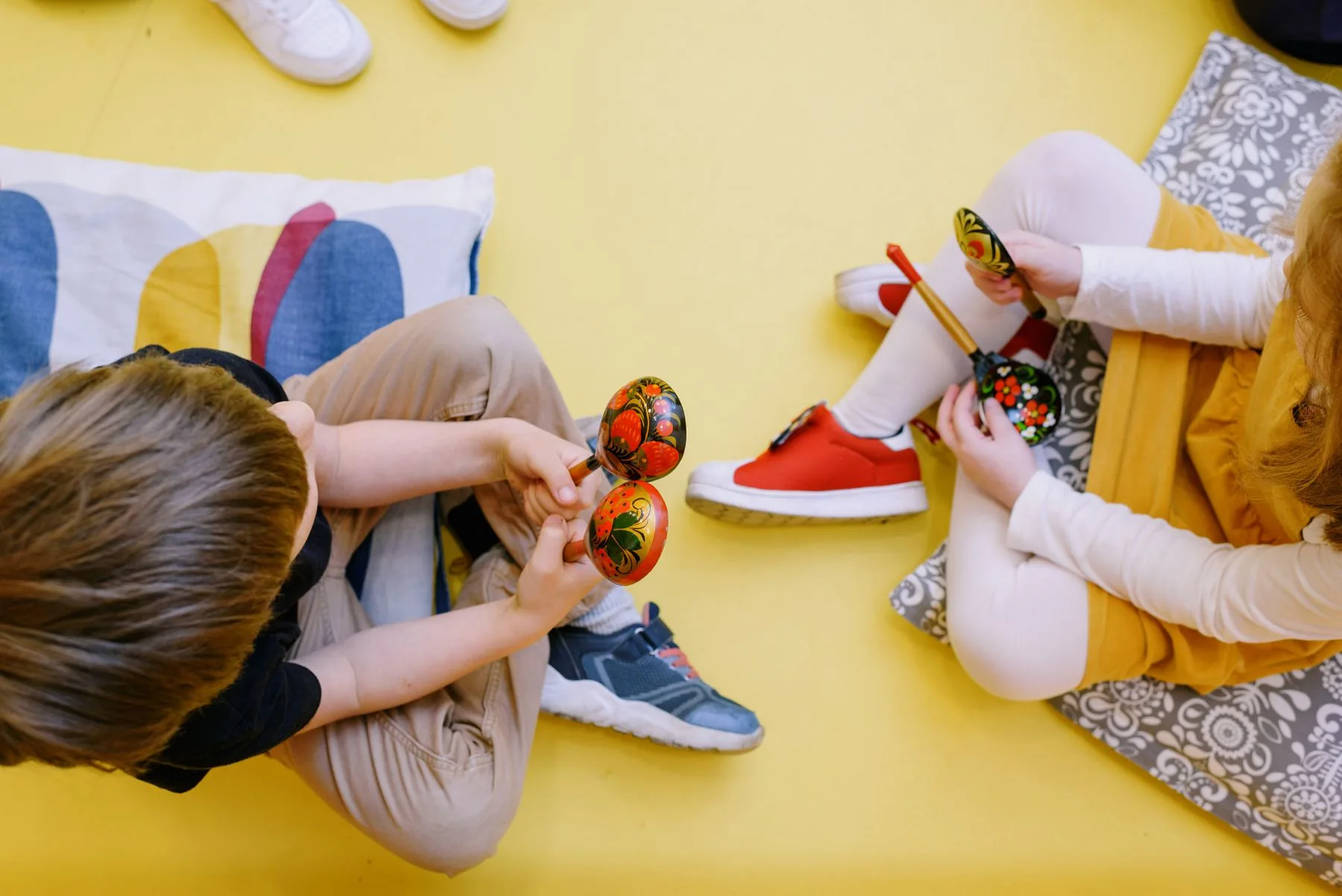 Vue de dessus de deux enfants assis, chacun tenant une paire de maracas en bois peintes de motifs colorés