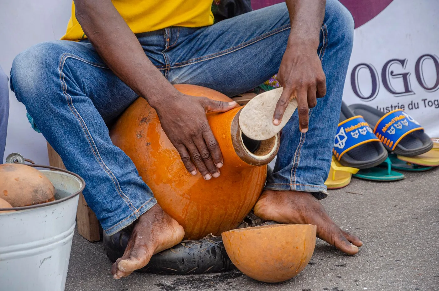 Un artisan évide une calebasse à la main, un morceau découpé posé à côté