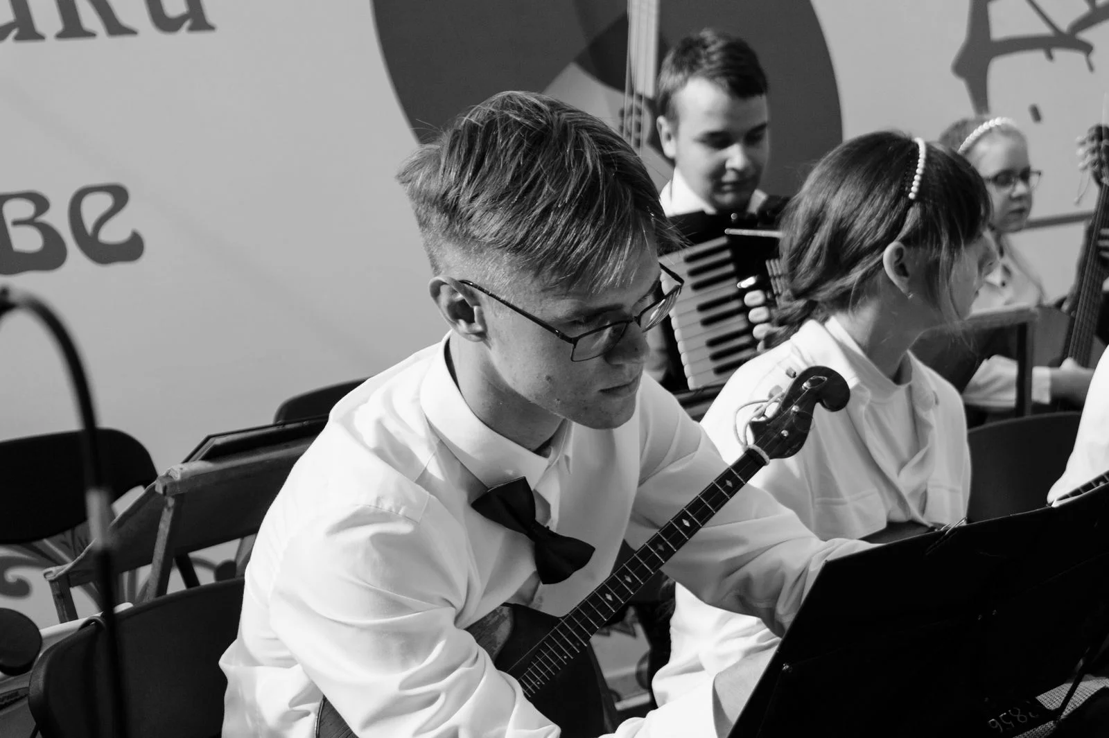 Jeune musicien jouant de la balalaika lors d un evenement appele Jour de la balalaika, entoure d autres musiciens dont un accordeoniste