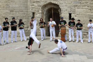 Joueur de berimbau tenant la verga et la cabaça devant une architecture en pierre lors d une roda de capoeira