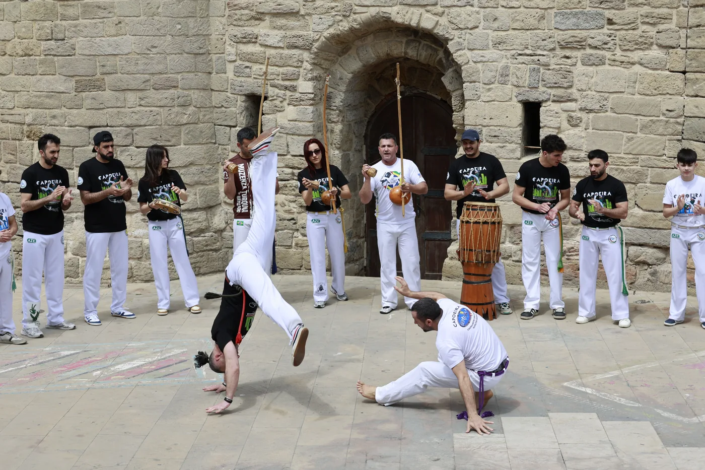 Joueur de berimbau tenant la verga et la cabaça devant une architecture en pierre lors d une roda de capoeira