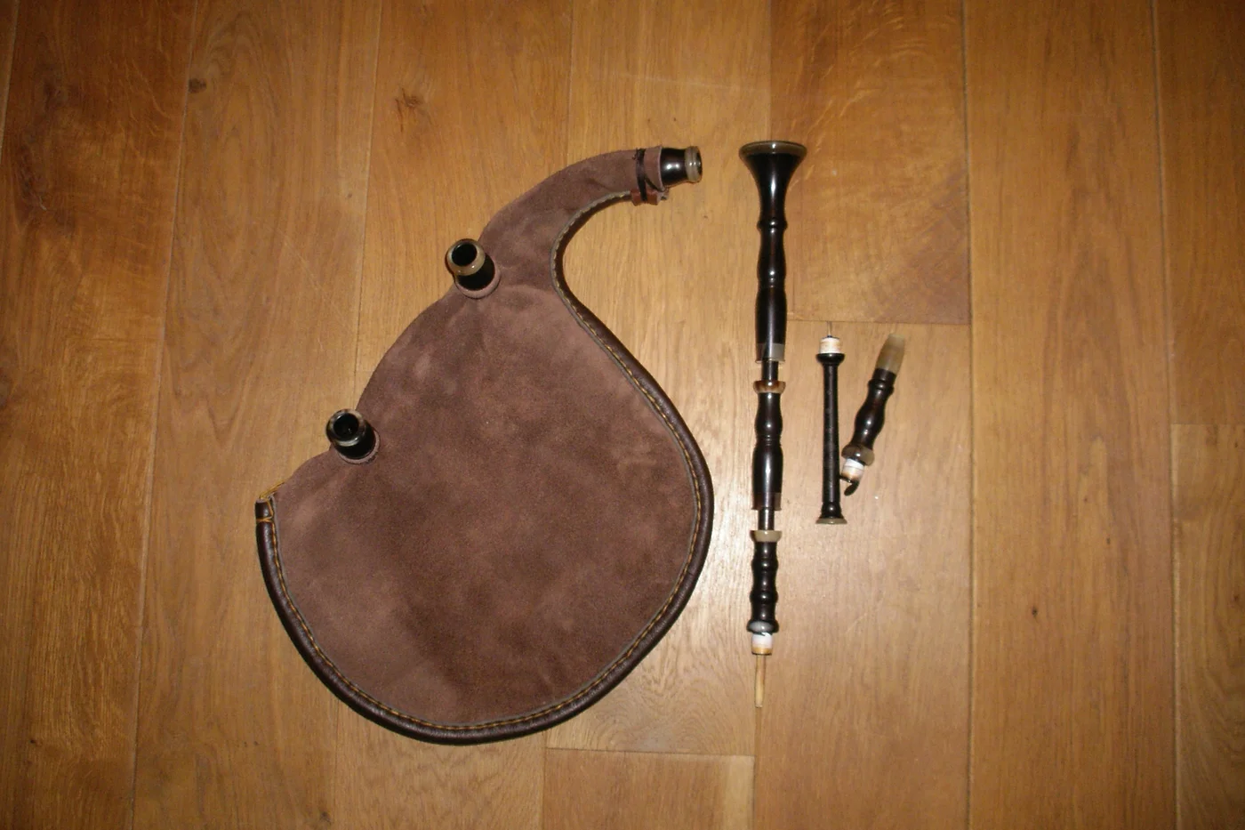 Biniou kozh démonté en quatre parties : le sac en cuir, le chalumeau levriad, le bourdon korn-boud et le petit tube d'insufflation sutell, posés sur un parquet