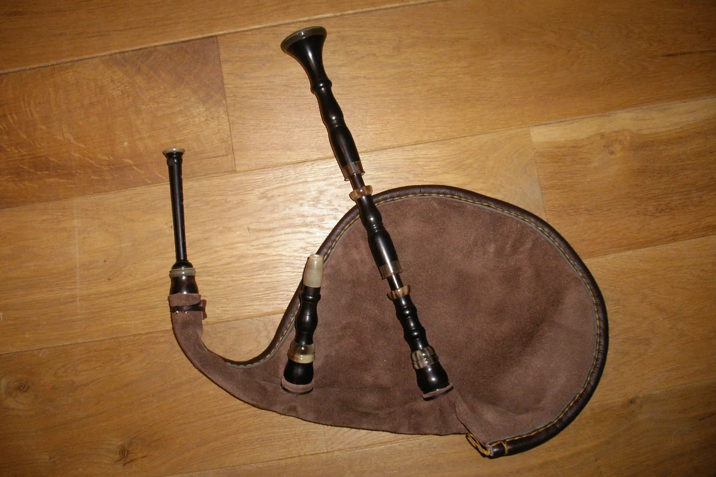 Biniou kozh assemblé, sac en cuir marron et chalumeau en bois sombre, posé sur un parquet