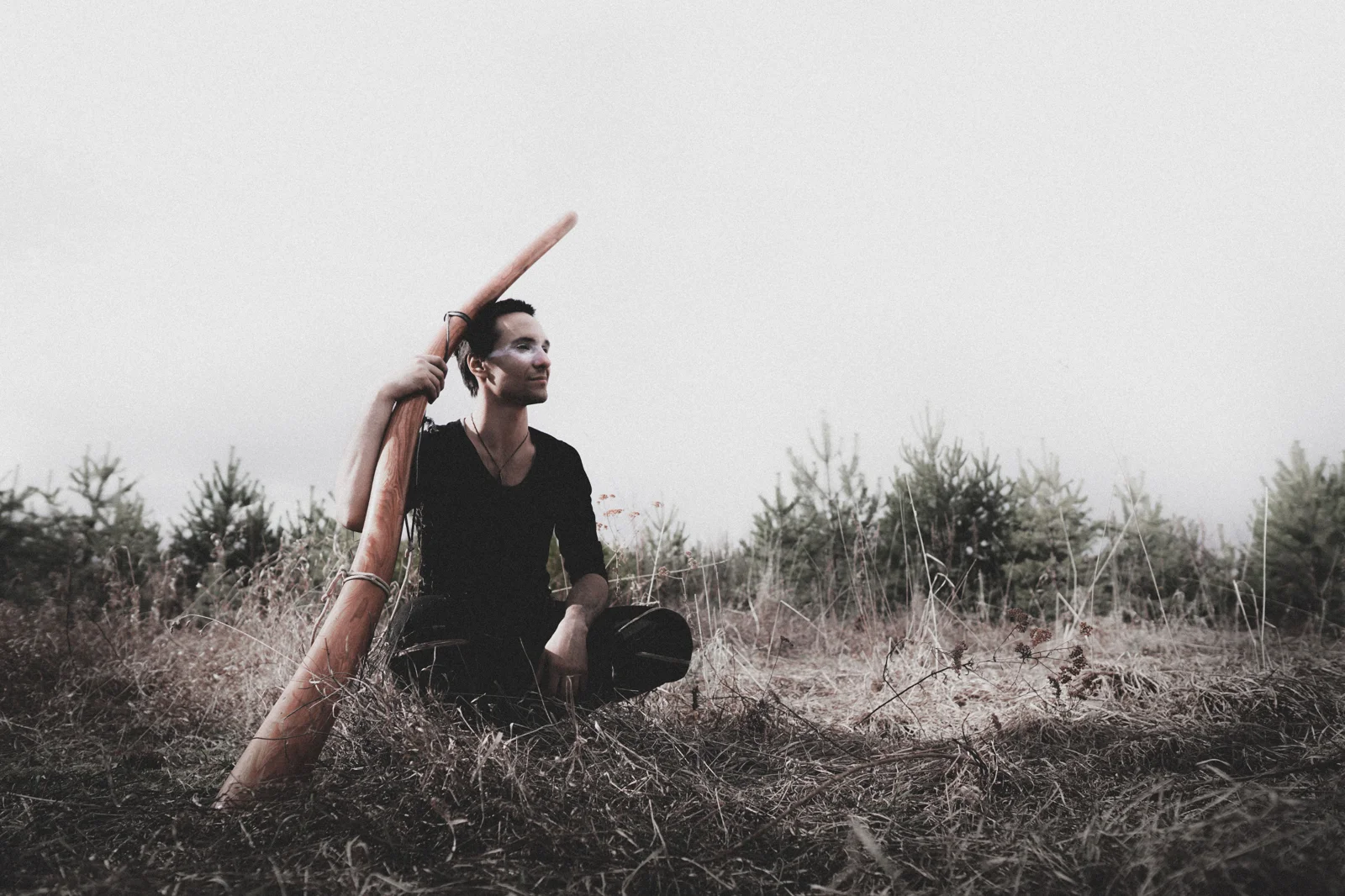 Un homme tient verticalement un long didgeridoo en bois, de forme conique