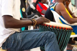 Un homme assis joue du djembé dans la rue, corde de tension et peau visibles