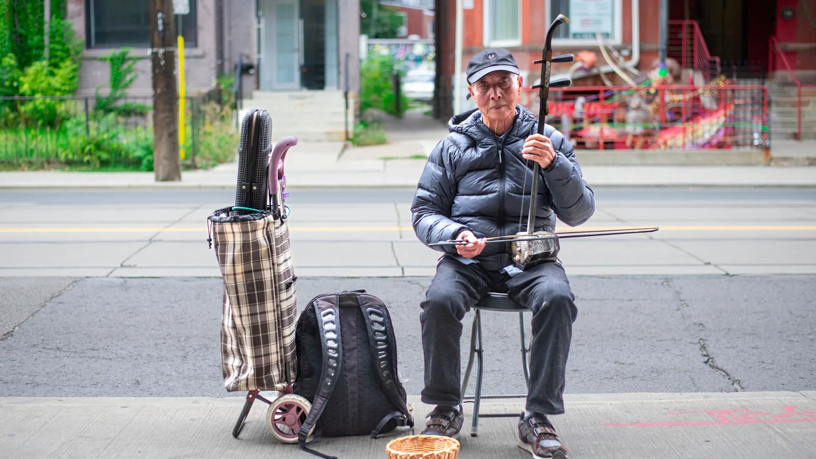 Musicien age jouant de l'erhu assis sur un trottoir en ville, la caisse hexagonale de l'instrument bien visible
