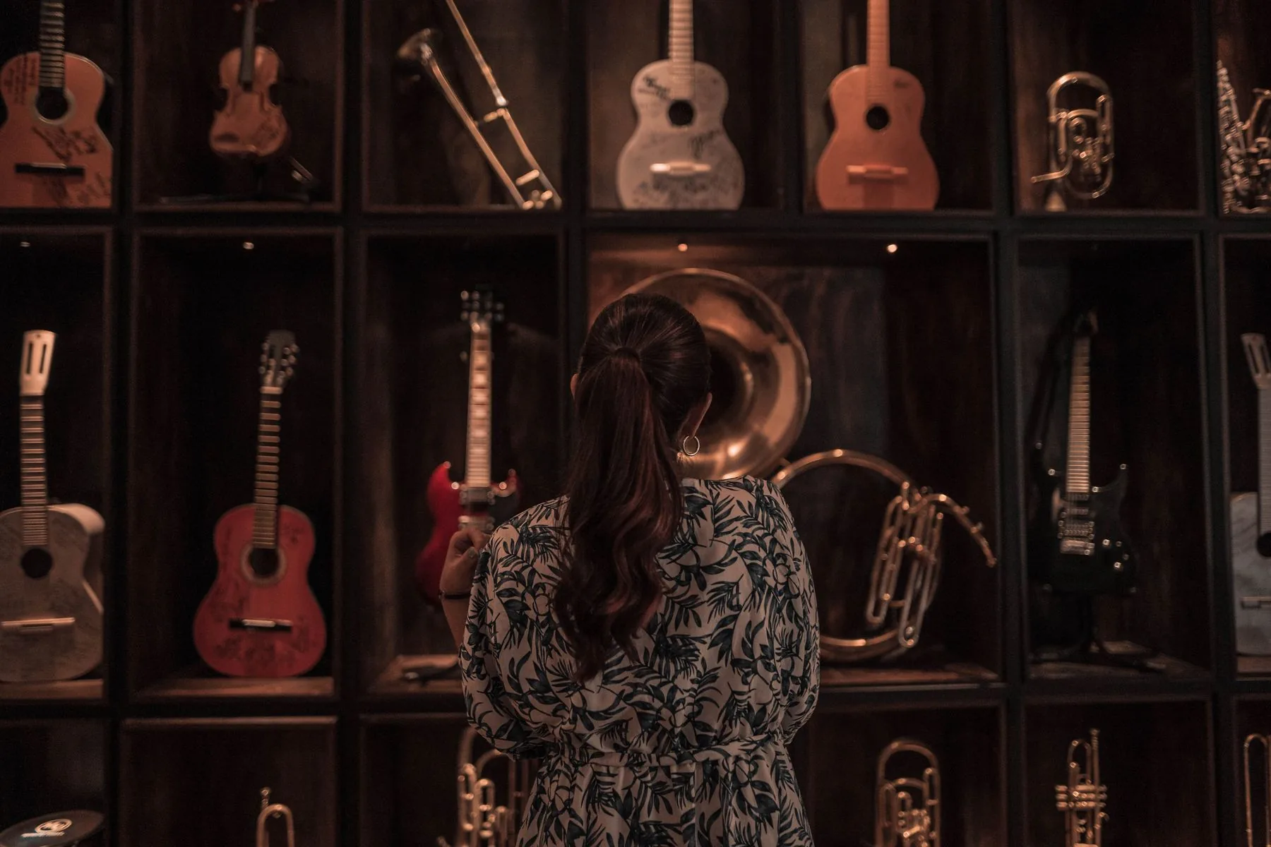 Une visiteuse observe un mur de guitares, violons, cuivres et instruments exposés dans des casiers de bois