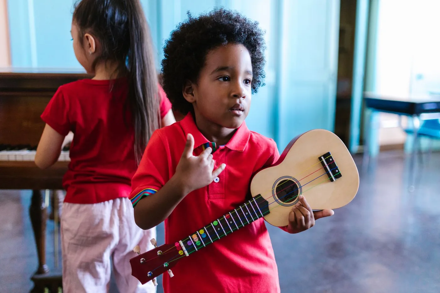 Un enfant tient un ukulélé pendant une animation musicale, une autre enfant joue du piano en arrière-plan
