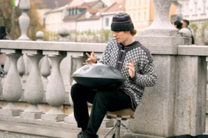 Musicien jouant du handpan assis sur la rambarde d un pont en pierre dans une ville europeenne