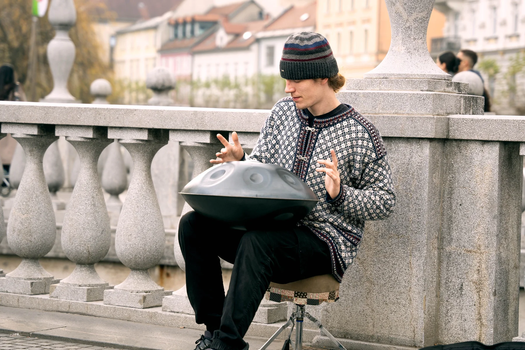 Musicien jouant du handpan assis sur la rambarde d un pont en pierre dans une ville europeenne