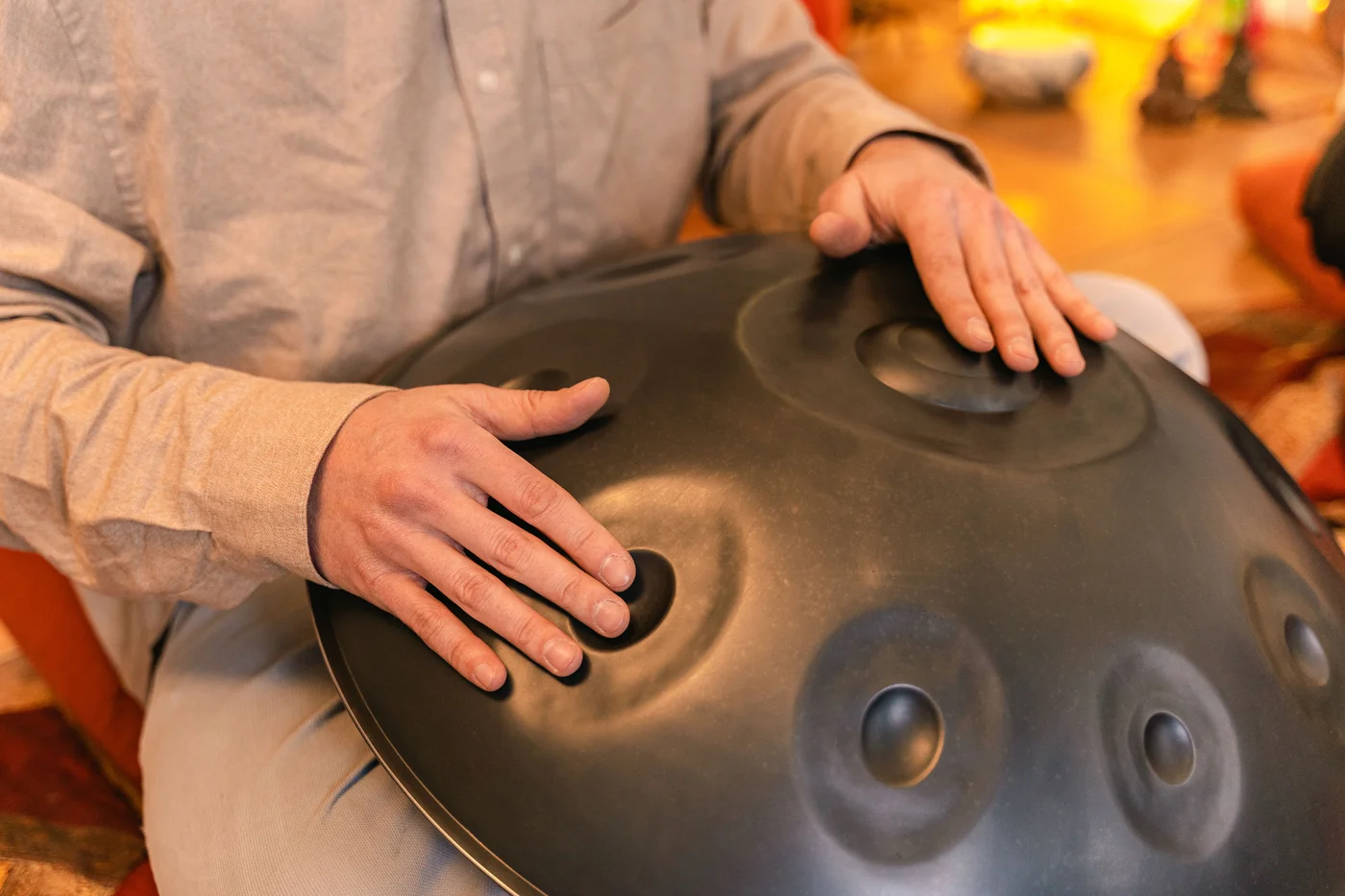 Gros plan sur les mains d'un musicien posées sur les champs de note bombés d'un handpan