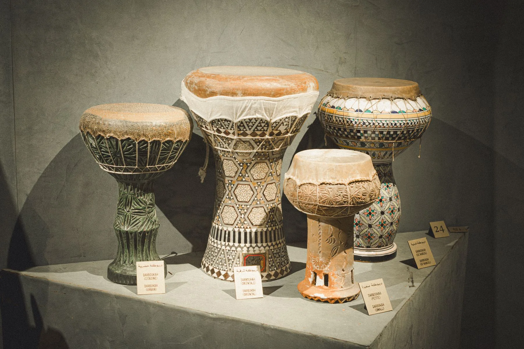 Cinq darboukah de tailles et décors différents, exposées avec leurs étiquettes dans une vitrine de musée