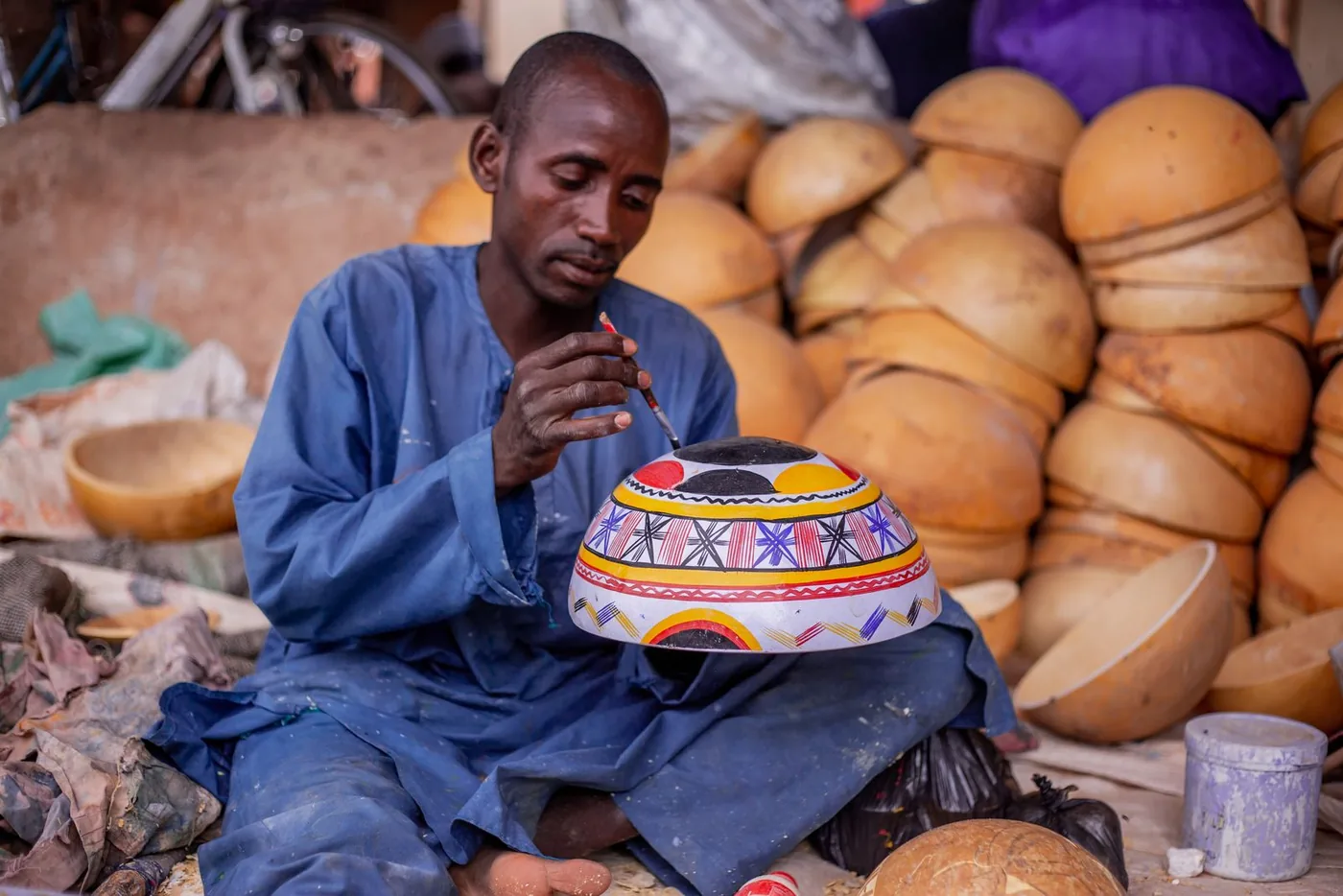 Un artisan peint une calebasse décorative, entouré d'une pile de calebasses