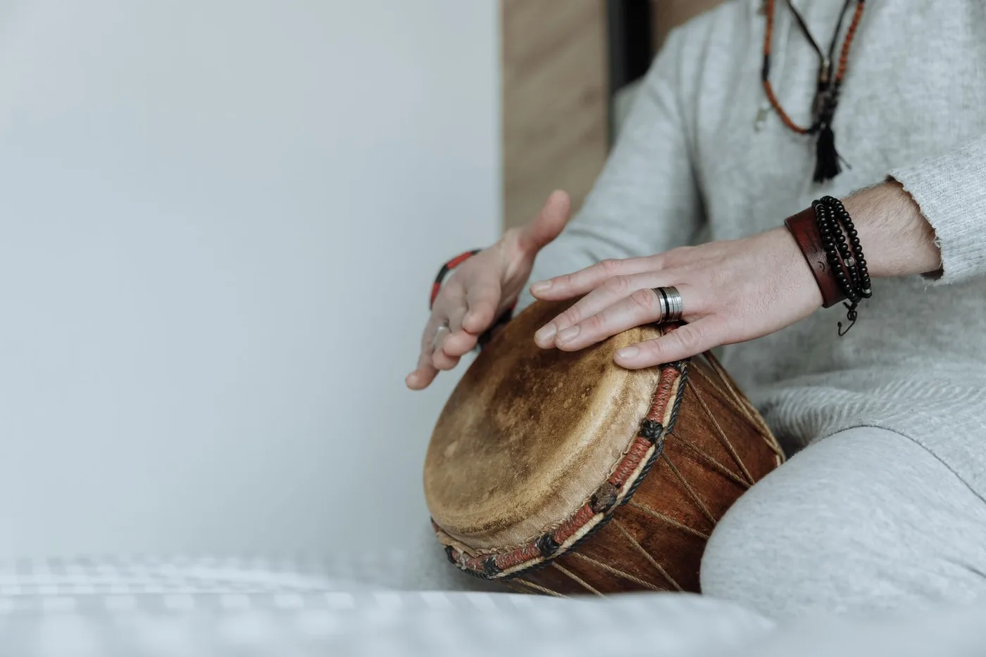 Deux mains posées sur la peau tendue d'un djembé, corde de tension visible