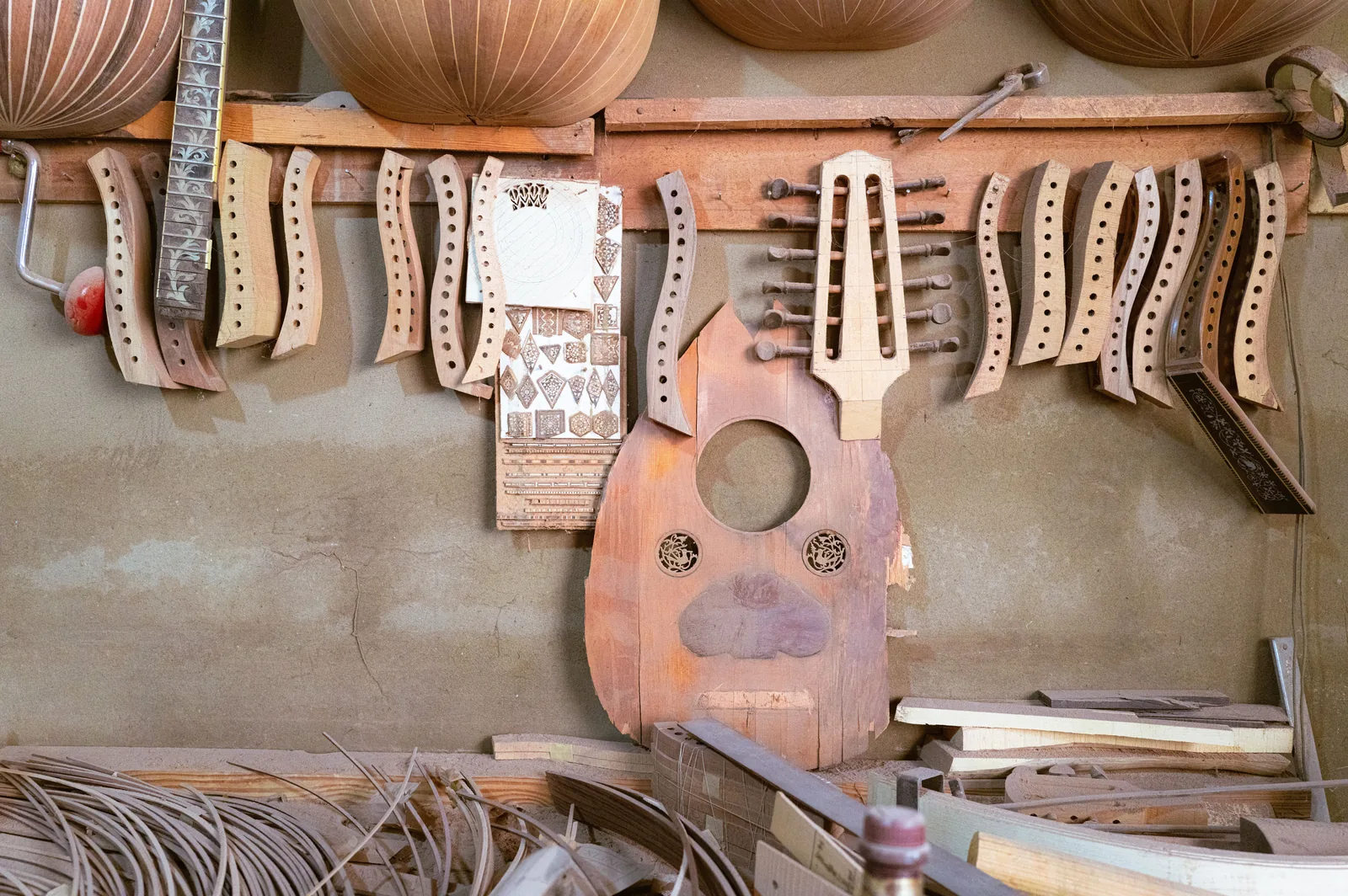 Pièces détachées d'un oud en cours de fabrication dans un atelier de lutherie, caisse et manches accrochés au mur