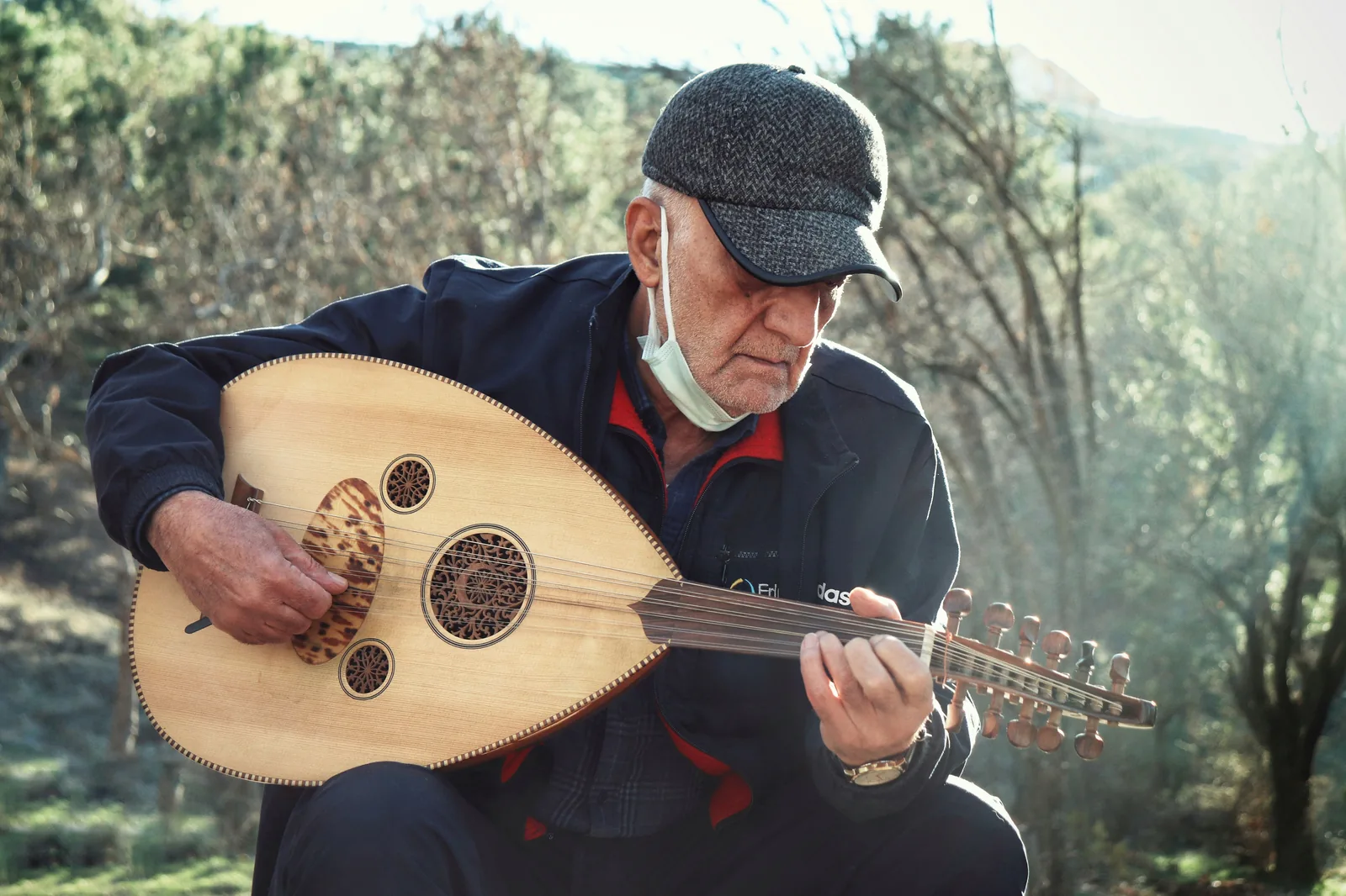 Musicien jouant du oud en extérieur, instrument tenu contre la poitrine, chevillier coudé visible